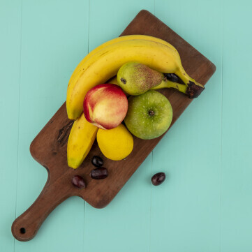 top view fruits as banana apple lemon peach grape berries cutting board blue background with copy space 1